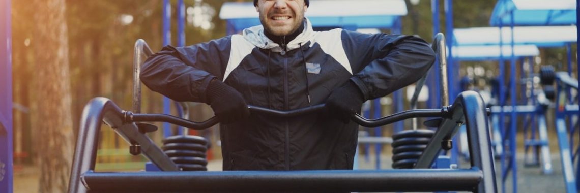Attractive young man doing exercise in outdoor gym in winter park